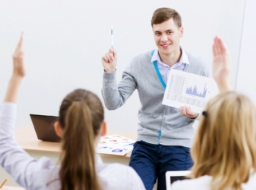 Male student teacher at the front of the class with two students with the hand up to answer a question