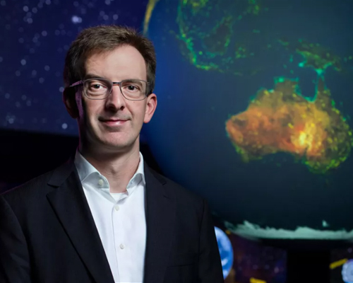 Associate Professor Gottfried Lechner standing next to globe of planet Earth