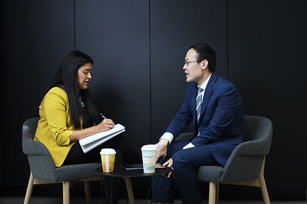 Two people sitting opposite each other talking while one takes notes in a book