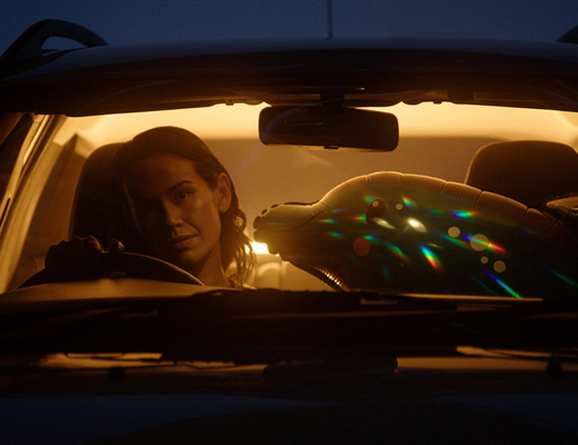 Woman driving a car at dusk, with an inflatable dolphin in the front passenger seat