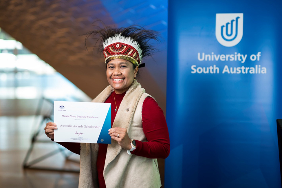 Monita wearing a traditional cassowary feather headdress from her hometown of Biak, Papua with her Australia Awards certificate in UniSA’s Pridham Hall.