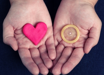 Two hands showing a stone heart and a condom