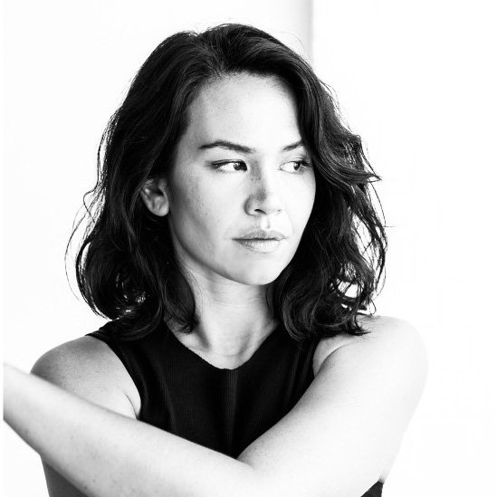 Black and white portrait of Amrita Hepi with her arm wrapped around her opposite shoulder. Amrita is an Aboriginal and Māori woman with shoulder length wavy hair wearing a black sleeveless top.jpg