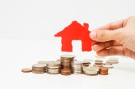 hand holding cut-out house over pile of coins