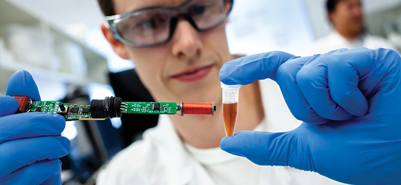 A researcher holding an electronic probe to a vial of liquid