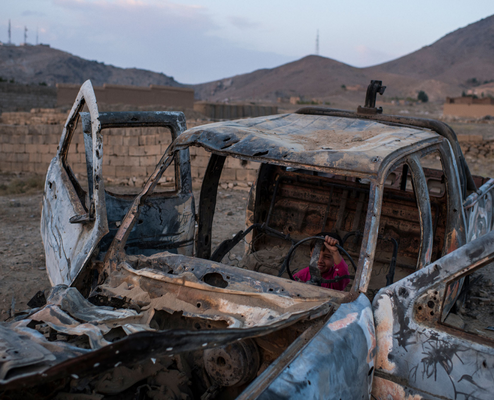 Photography, Andrew Quilty. A boy from plays in the burnt-out remains of a former Afghan National Police Ranger vehicle. The vehicle was being driven by Taliban fighters when it was destroyed by an airstrike around the time the Taliban took control of Kabul, which is an hour's drive further north.