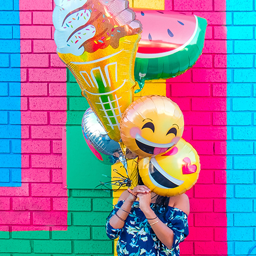 woman holding smiley balloons in front of her face