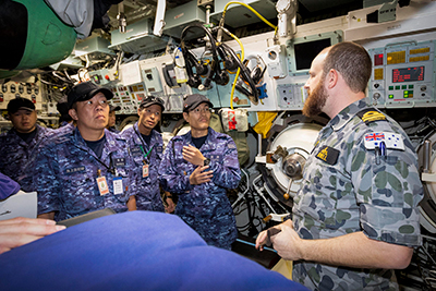Royal Australian Navy officer Lieutenant Joseph Howell (right) explains the weapon storage compartment to Japan Maritime Self-Defense Force personnel during a tour of HMAS Sheean as part of Exercise Pacific Reach at Fleet Base West, Western Australia. Photo by Royal Australian Navy.