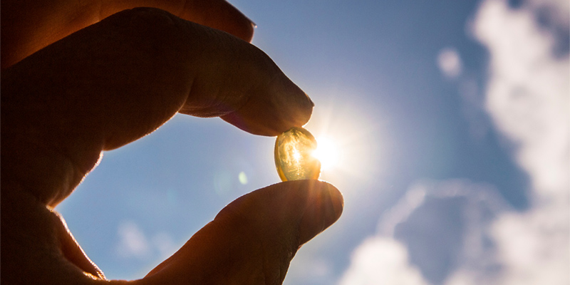 Hand holding a vitamin D capsule up to the sun